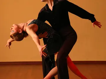 Ein Tanzpaar führt eine elegante Figur auf: Der Mann hält die Frau, die sich mit nach hinten gebeugtem Oberkörper in seine Arme legt.