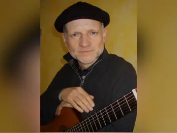 Oliver König, auf seine Gitarre gestützt vor einem gelben Hintergrund