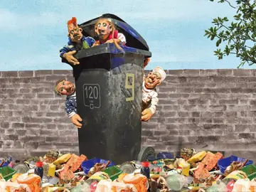 Vier Puppenfiguren schauen aus einer großen grauen 120-Liter-Mülltonne hervor, die vor einer Backsteinmauer steht. Oben sitzen der Junge mit orangefarbenen Haaren und das Mädchen mit Zöpfen; an den Seiten hängen die ältere Dame und der Mann in Arbeitskleidung. Vor der Mülltonne liegt ein großer Haufen gemischter Müll wie Dosen, Plastik, Essensreste und Verpackungen.