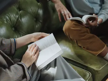 Zwei Personen sitzen auf einem grünen Ledersofa und lesen jeweils in einem aufgeschlagenen Buch.