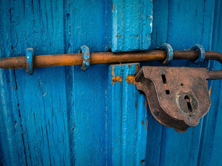 Eine blaue Holztür mit einem alten rostigen Schloss davor