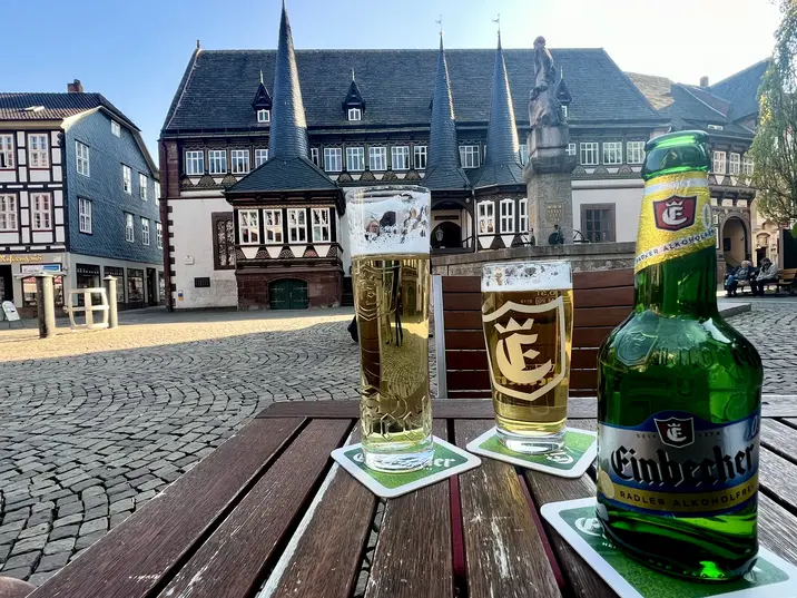 Blick aufs das alte Rathaus Einbeck und den Brunnen auf dem Vorplatz. Im Vordergrund ist eine Flasche Einbecker Radler alkoholfrei und zwei Gläser mit Bier zu sehen.