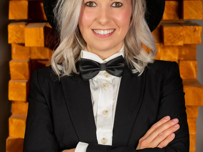 Eine blonde Sängerin im schwarzen Anzug mit Fliege und Hut lächelt in die Kamera