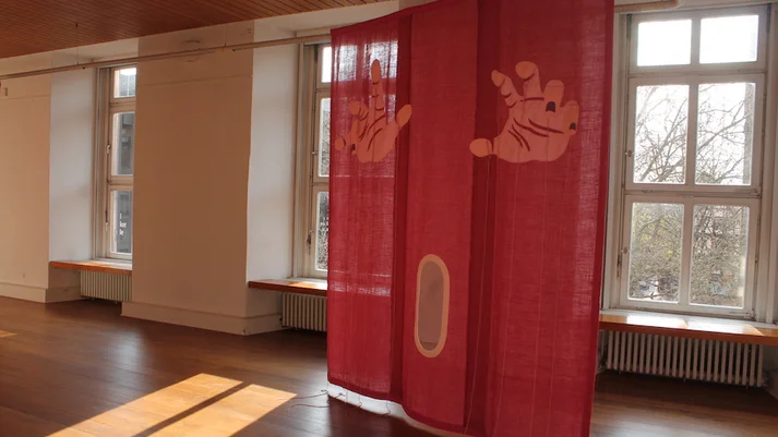 Ausstellungsraum mit einer Installation aus rotem Stoff und darauf abgebildeten Händen