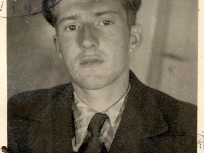 Schwarzweiß-Fotografie eines jungen Mannes im Anzug und Krawatte, der ernst in die Kamera blickt. Das Foto zeigt leichte Gebrauchsspuren und ist an den Ecken mit Heftklammern befestigt