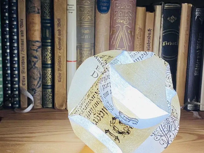 Leuchtende Papierkugel vor einem Hintergrund aus alten Büchern